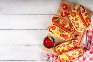 Lezzetli gurme pizza sosisleri sosisli, sosisli, domatesli, peynirli, biberli, kirazlı, domatesli ve otlu, beyaz ahşap masadaki sosisli ve sosisli ve pizzanın popüler kombinasyon tarifi.