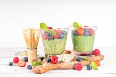 Bir gecelik yulaf ezmesi, yoğurtlu veya sütsüz tatlı yulaf, taze çilek, yabanmersini, ahududu ve nane ile birlikte beyaz ahşap mutfak masasında bulunan malzemeler.