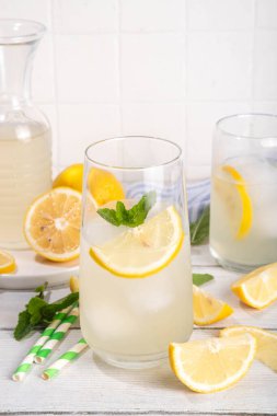 Buzlu ev yapımı limonata, naneli limonlu limonata kokteyli ve beyaz ahşap mutfak arka planında limonlar.