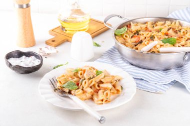 Son moda viral benimle tavuk makarnası evlen. Bir tencere yumuşak makarna ve kremalı ve peynirli sulu tavuk parçaları, sarımsaklı güneşte kurutulmuş domates sosu, nükteli fesleğen yaprağı, tabak ve demlikte.