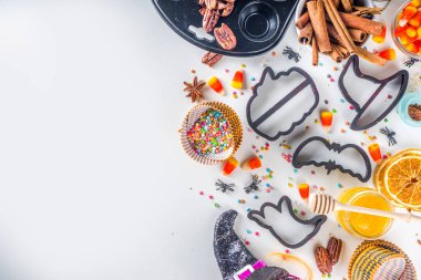 Cadılar Bayramı zencefilli kurabiye pişirme arka planı. Sonbahar tatili pişirme konsepti, malzemeler, baharatlar, cadılar bayramı sembolü kurabiye kesiciler - balkabağı, hayalet, yarasa, cadı şapkası, üst görünüm beyaz masa kopyalama alanı