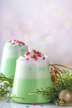 Yeşil kibrit Noel lattesi, krema ve şeker serpiştirilmiş, yeni yıl tatili dekore edilmiş arka planda.