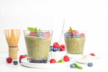 Sağlıklı kahvaltılık chia pudingi, yanında matcha latte çayı ve bardakta taze yaz meyvesi, beyaz arka plan fotokopi alanı.