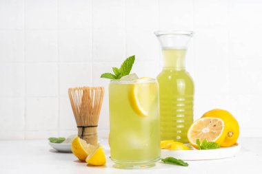 Buzlu Matcha Limonata kokteyli. Yeşil buzlu kibrit çayı, limon dilimleri ve beyaz arka planda taze nane ile karıştırılmış içecek. 