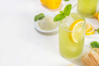 Buzlu Matcha Limonata kokteyli. Yeşil buzlu kibrit çayı, limon dilimleri ve beyaz arka planda taze nane ile karıştırılmış içecek. 