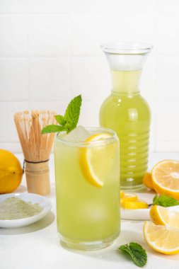 Buzlu Matcha Limonata kokteyli. Yeşil buzlu kibrit çayı, limon dilimleri ve beyaz arka planda taze nane ile karıştırılmış içecek. 