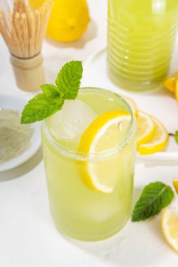 Buzlu Matcha Limonata kokteyli. Yeşil buzlu kibrit çayı, limon dilimleri ve beyaz arka planda taze nane ile karıştırılmış içecek. 