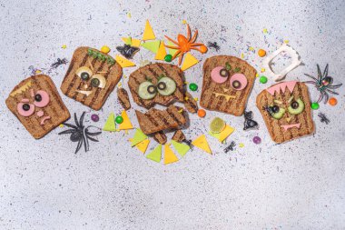 Funny halloween monster sandwiches. Set of various decorated monster sandwich and toasts, with cucumber, cheese and meat sausages, white table background with Halloween decorations