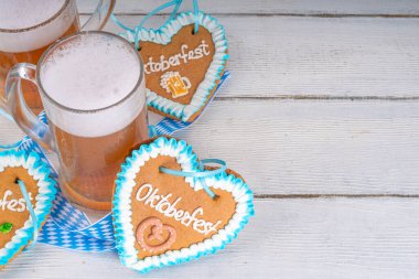 Oktoberfest davetiyesi, menü, tebrik kartı, bira bardaklı beyaz ahşap masa, eklem festivali sembollü kareli kurdele ve kalp kurabiyeleri - çiçek, bira, kraker üst görünümü