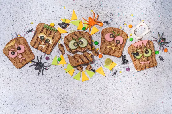 Funny halloween monster sandwiches. Set of various decorated monster sandwich and toasts, with cucumber, cheese and meat sausages, white table background with Halloween decorations