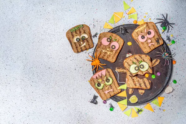 Funny halloween monster sandwiches. Set of various decorated monster sandwich and toasts, with cucumber, cheese and meat sausages, white table background with Halloween decorations