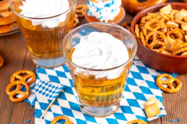 Oktoberfest tatlı fikri, üzerinde krem şanti olan renkli biralı iki bardak altın jöle pudingi, şenlikli Oktoberfest partisi ahşap masa, kopyalama alanı.