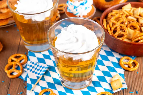 Oktoberfest tatlı fikri, üzerinde krem şanti olan renkli biralı iki bardak altın jöle pudingi, şenlikli Oktoberfest partisi ahşap masa, kopyalama alanı.