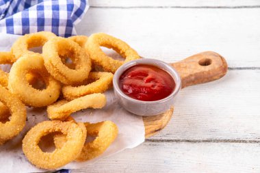 Ketçap soslu altın soğan halkaları, uçak fritözü beyaz ahşap masa fotokopi alanında lezzetli soğan halkaları atıştırmalıkları.