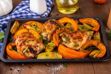 Kavrulmuş fırında tavuk budu, balkabağı ve patates dilimleri, sarımsak ve aromalı bitkiler. Lezzetli sonbahar konforlu yemekleri, Şükran Günü aile yemeği fikirleri.