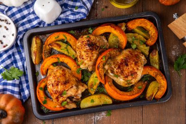 Kavrulmuş fırında tavuk budu, balkabağı ve patates dilimleri, sarımsak ve aromalı bitkiler. Lezzetli sonbahar konforlu yemekleri, Şükran Günü aile yemeği fikirleri.