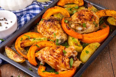 Kavrulmuş fırında tavuk budu, balkabağı ve patates dilimleri, sarımsak ve aromalı bitkiler. Lezzetli sonbahar konforlu yemekleri, Şükran Günü aile yemeği fikirleri.