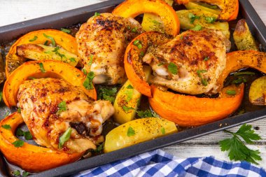 Kavrulmuş fırında tavuk budu, balkabağı ve patates dilimleri, sarımsak ve aromalı bitkiler. Lezzetli sonbahar konforlu yemekleri, Şükran Günü aile yemeği fikirleri.