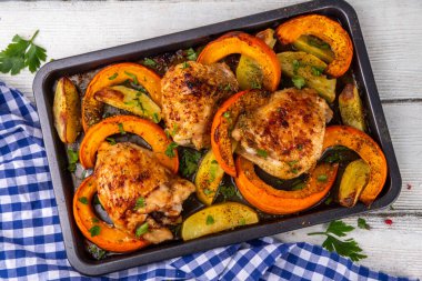 Kavrulmuş fırında tavuk budu, balkabağı ve patates dilimleri, sarımsak ve aromalı bitkiler. Lezzetli sonbahar konforlu yemekleri, Şükran Günü aile yemeği fikirleri.