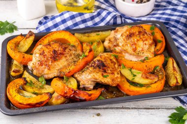 Kavrulmuş fırında tavuk budu, balkabağı ve patates dilimleri, sarımsak ve aromalı bitkiler. Lezzetli sonbahar konforlu yemekleri, Şükran Günü aile yemeği fikirleri.