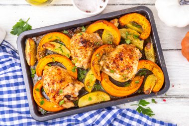 Kavrulmuş fırında tavuk budu, balkabağı ve patates dilimleri, sarımsak ve aromalı bitkiler. Lezzetli sonbahar konforlu yemekleri, Şükran Günü aile yemeği fikirleri.