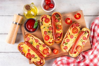 Lezzetli gurme pizza sosisleri sosisli, sosisli, domatesli, peynirli, biberli, kirazlı, domatesli ve otlu, beyaz ahşap masadaki sosisli ve sosisli ve pizzanın popüler kombinasyon tarifi.