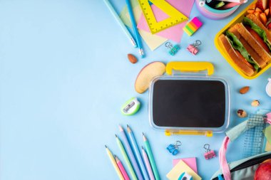 Okula dönelim. Sağlıklı okul yemekleri, çocuklar beslenme çantasına meyve, böğürtlen, fındık ve sebzeli sandviç koydu. Çocukların diyet yemekleri, eğitim okulu malzemeleri, parlak mavi arka plan manzarası.