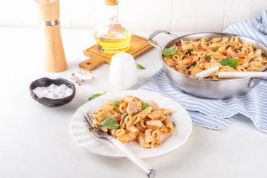 Son moda viral benimle tavuk makarnası evlen. Bir tencere yumuşak makarna ve kremalı ve peynirli sulu tavuk parçaları, sarımsaklı güneşte kurutulmuş domates sosu, nükteli fesleğen yaprağı, tabak ve demlikte.