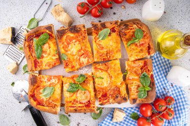 Domates ve fesleğenli ev yapımı margarita pizza, malzemeler ve arka planda beyaz mutfak masasında zeytinyağı.