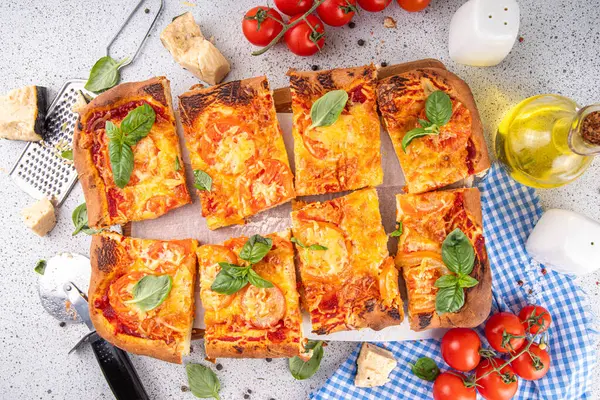 Domates ve fesleğenli ev yapımı margarita pizza, malzemeler ve arka planda beyaz mutfak masasında zeytinyağı.