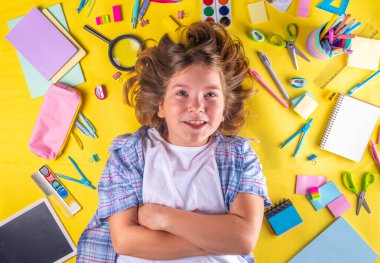 Sevimli duygusal kız okula dönmeye hazır çeşitli okul malzemeleriyle, parlak sarı arka planda eğitim aksesuarlarıyla.