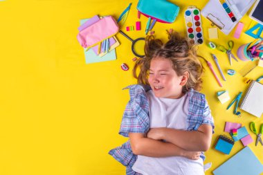 Sevimli duygusal kız okula dönmeye hazır çeşitli okul malzemeleriyle, parlak sarı arka planda eğitim aksesuarlarıyla.