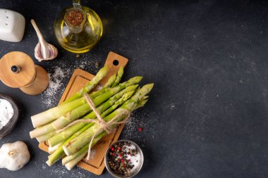 Çiğ organik kuşkonmaz mutfak masasının arka planında bir sürü ev yapımı yeşil kuşkonmaz pişirmeye ve kesme tahtasının üzerinde hazır. Yaz hasadı, yaz yemeği malzemeleri.