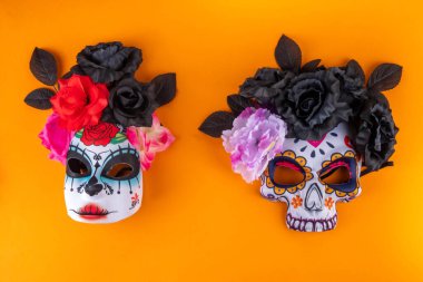 Dia de los muertos holiday background with black autumn flowers, and Mexican Day of the Dead carnival masks. on bright orange background copy space
