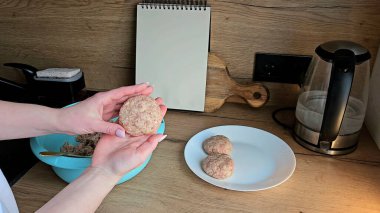 Mutfak ortamında kıyma köftelerini şekillendiren eller, ahşap bir yüzey üzerinde tabak ve kâse.. 