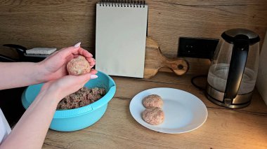 Mutfak ortamında kıyma köftelerini şekillendiren eller, ahşap bir yüzey üzerinde tabak ve kâse.. 