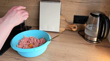 Eller mutfak tezgahında bir kase kıymalı ete yumurta kırıyor. Kurulum yemek hazırlama sahnesini içeriyor..