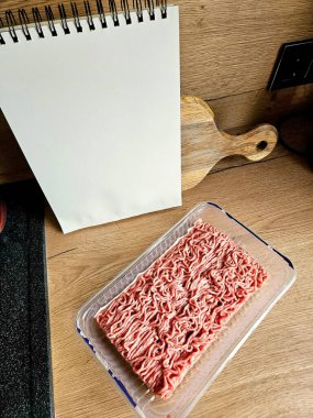  Boş spiral kaplı not defteri tahta bir yüzey üzerinde çiğ et tepsisinin yanında dikiliyor.