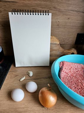 Yemek tarifi için gereken malzemeler arasında açık bir defter, kasede kıyma, iki yumurta, bütün bir soğan ve sarımsaklı karanfil bulunur..