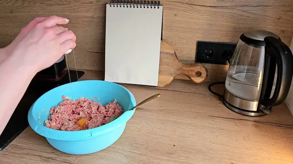 Eller mutfak tezgahında bir kase kıymalı ete yumurta kırıyor. Kurulum yemek hazırlama sahnesini içeriyor..