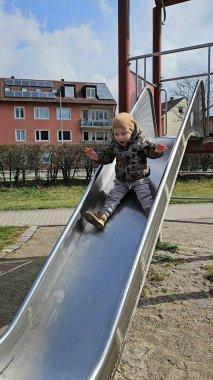 Metal bir oyun parkından kayan çocuk sıcak bir ceket ve bereyle meskun binalarla çevrili bir şekilde neşeyle kayıyor. Yüzlerinde heyecan ve mutluluğun ifadesi
