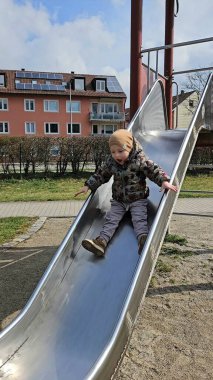 Metal bir oyun parkından kayan çocuk sıcak bir ceket ve bereyle meskun binalarla çevrili bir şekilde neşeyle kayıyor. Yüzlerinde heyecan ve mutluluğun ifadesi