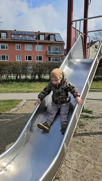 Metal bir oyun parkından kayan çocuk sıcak bir ceket ve bereyle meskun binalarla çevrili bir şekilde neşeyle kayıyor. Yüzlerinde heyecan ve mutluluğun ifadesi