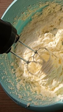 Mavi bir kasede tereyağlı krema karıştırıcı görüntüsü. Yumuşak, kremsi dokular karışımın bileşenleri birbirine kırbaçlayıp pişirme sürecinde bir anı yakaladığı gibi görünür.