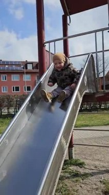 Metal bir oyun parkından kayan çocuk sıcak bir ceket ve bereyle meskun binalarla çevrili bir şekilde neşeyle kayıyor. Yüzlerinde heyecan ve mutluluğun ifadesi