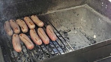 Izgara sosisler mangal ızgarasında pişiyor, duman çıkarıyor ve ızgara izleri gösteriyor. Bu görüntü açık hava barbeküsünün özünü yakalar, yemek temalı içerik için mükemmeldir.