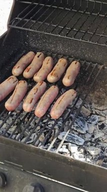 Izgaranın altında kömür közleri olan ızgarada ızgara edilmiş sosisler. Sahne, açık hava yemeklerinin özünü yakalar, ızgara sürecinin altını çizer.