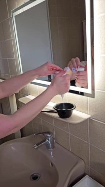 Elleri, banyo lavabosunun üzerine saç boyası dökerken görülmüş. Aynayla aksiyonu yansıtıyor. Sahne kişisel bakım ve bakım üzerine odaklanmıştır.