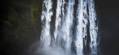 İzlanda 'da geniş bir Skgafoss şelalesi manzarası. Düşen su berrak ve parlak, yosunlu yeşil kenarları ise gölgelerle kaplı..