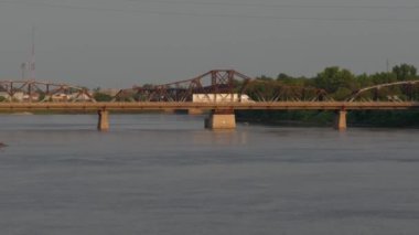 Sıcak bir yaz akşamında Winnipeg, Manitoba 'daki Kızıl Nehir' in manzarası. Uzaktan büyük bir kamyonun geçtiği bir araba köprüsü görülebilir. Büyük nehir gün batımının altında parlıyor, mavi.